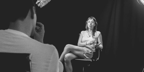A woman is being interviewed in a studio with black background and professional lighting.