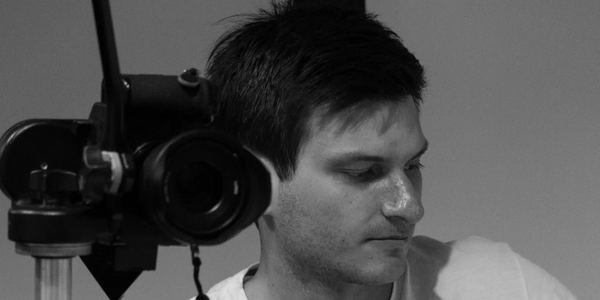 A man in a white shirt looks away beside a camera on a tripod.