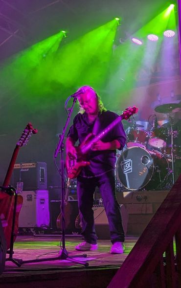 Musician playing bass guitar under vibrant green stage lights.