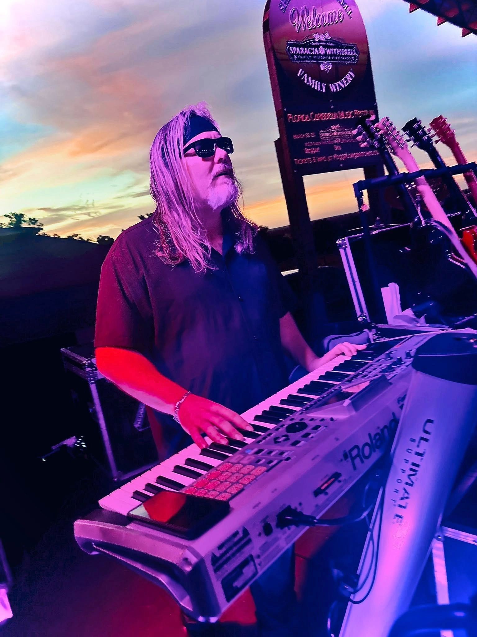 Musician playing keyboard at sunset with guitars nearby.