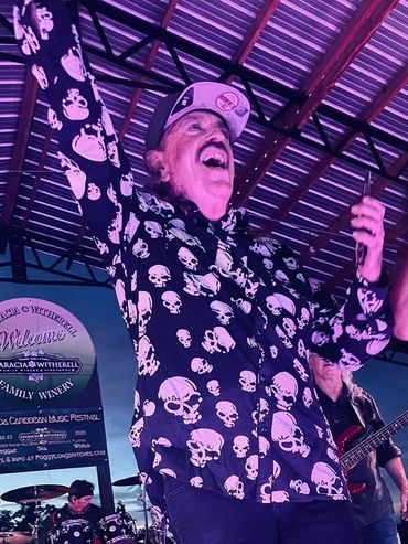 Two lively singers perform on stage with a band in the background.