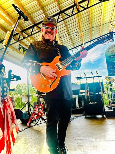 Smiling guitarist performing on stage under a yellow roof.