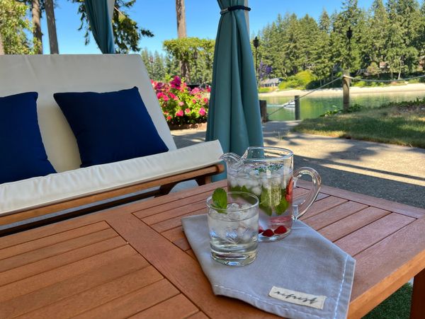 Refreshing drinks with mint and berries on a wooden table by a cozy outdoor lounge.