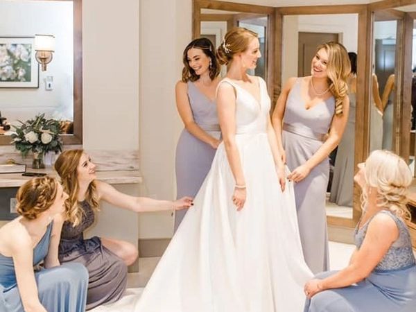 Bride surrounded by bridesmaids adjusting her wedding dress in a bright room.