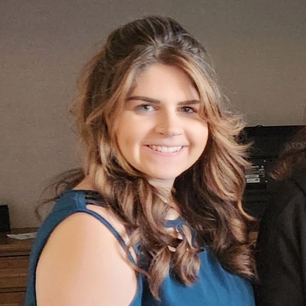 Smiling woman with wavy hair in a blue cold-shoulder top.