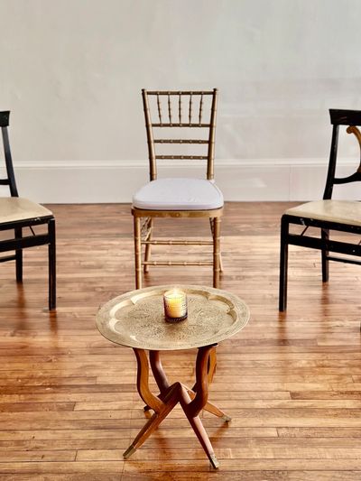 A small candle on a brass tray table with chairs in the background.