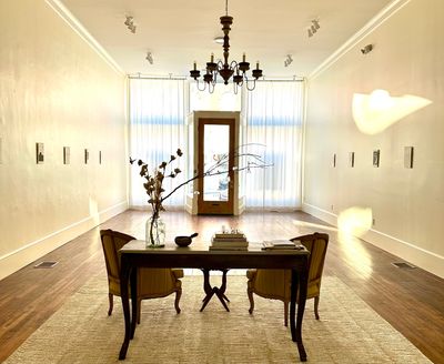 Two vintage French chairs and a console table in a serene gallery with a large chandelier
