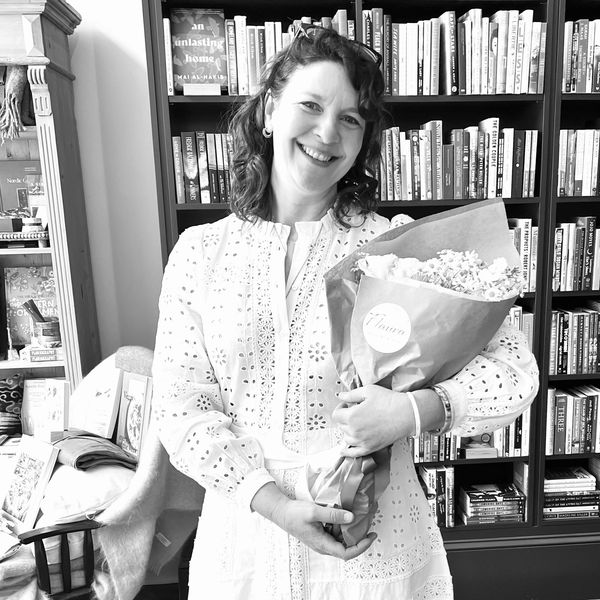 Smiling woman in a white dress holding a bouquet of flowers inside a bookshop