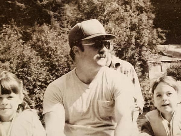 Man in sunglasses and cap with two children outdoors.