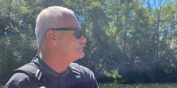 Man with gray hair and sunglasses in a sunny forest.