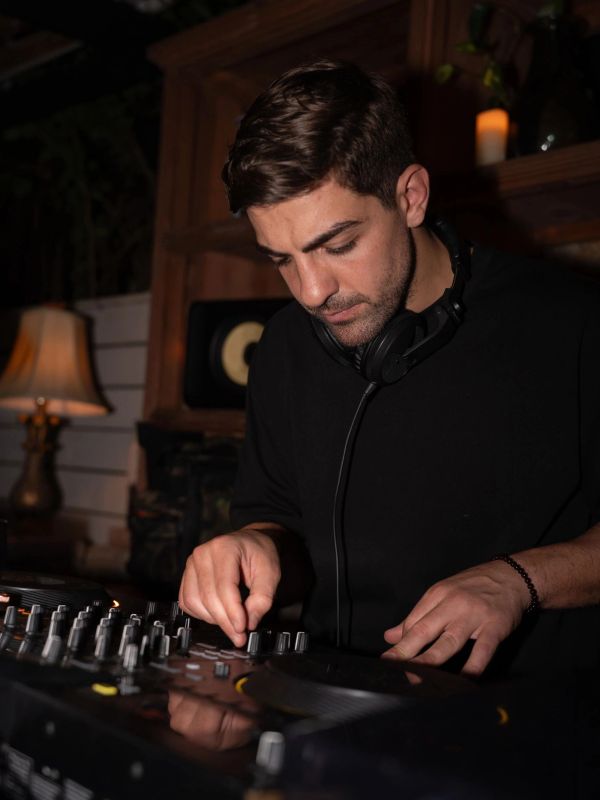 A DJ intently adjusting controls on his mixer with headphones around his neck.