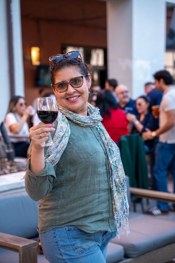 A smiling woman holding a glass of red wine, enjoying a social gathering.