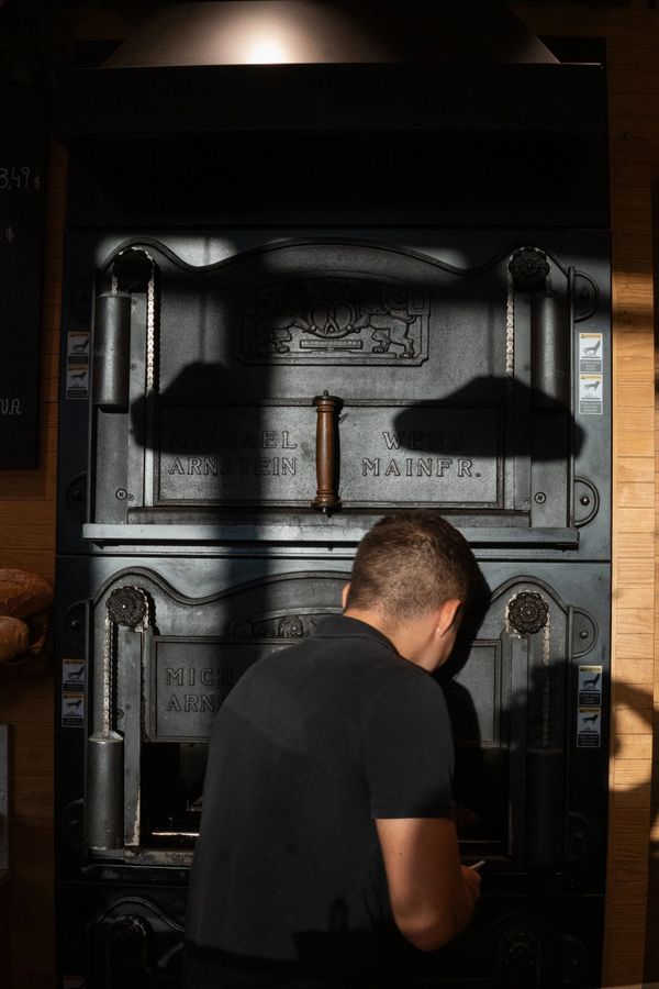 Man working in front of an old industrial oven with shadows cast on it.