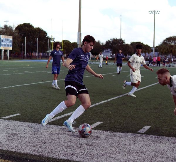 Soccer player in navy blue controlling the ball near the sideline during a match.