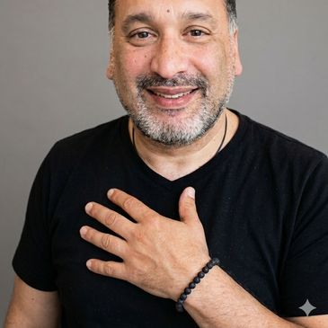 Man smiling with hand on chest wearing a black shirt and beaded bracelet.