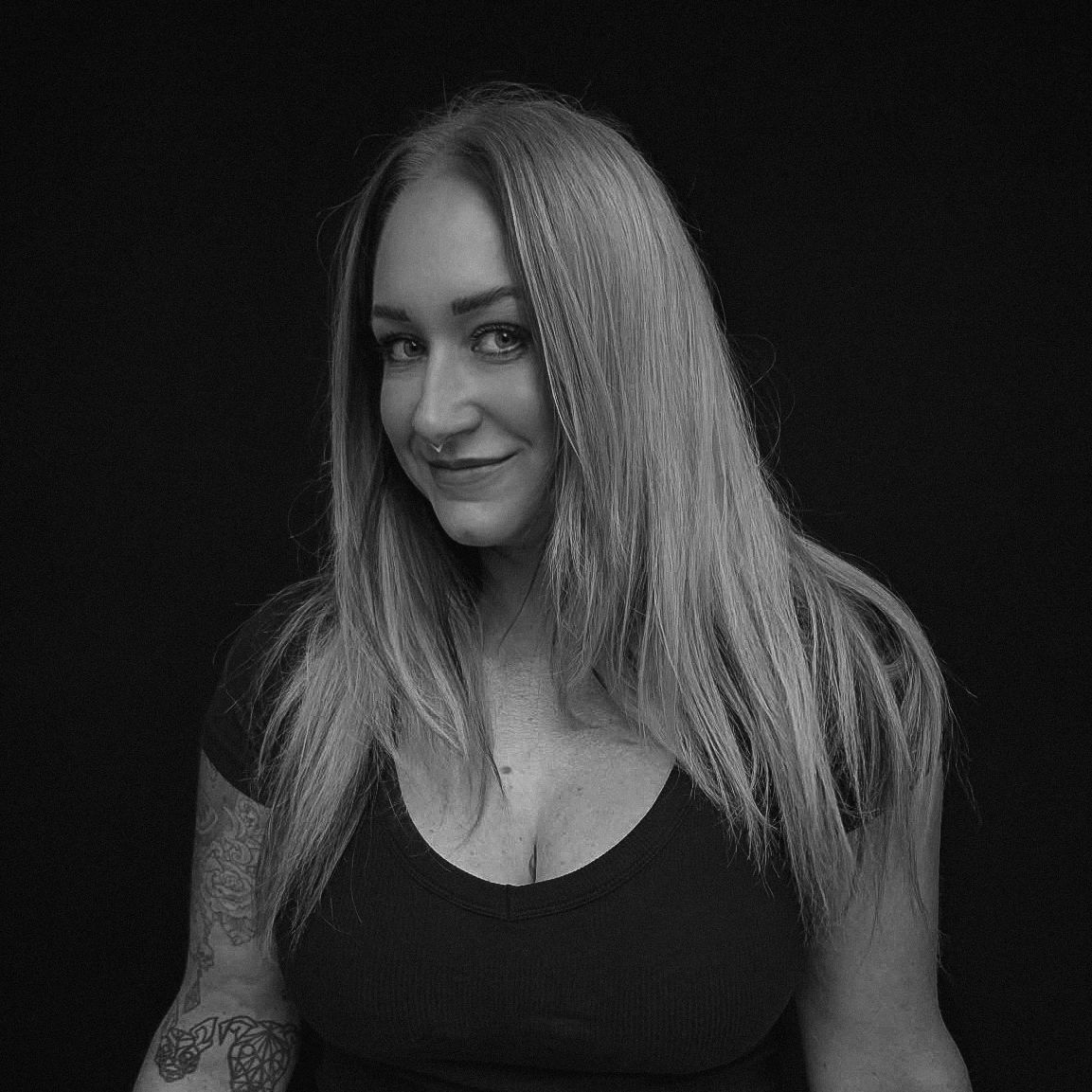 Black and white portrait of a smiling woman with long hair and tattoos.