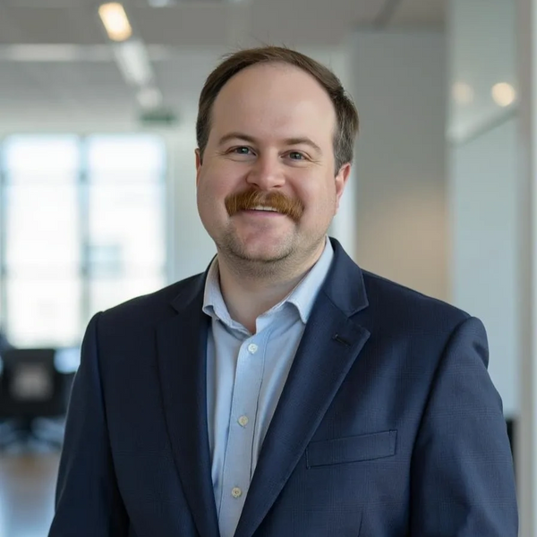 Smiling man with a mustache in a blue suit jacket.