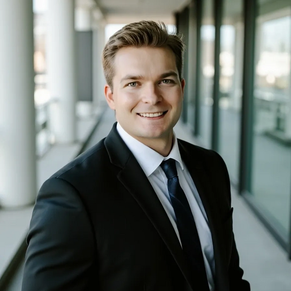 Confident young businessman in a black suit smiling indoors.