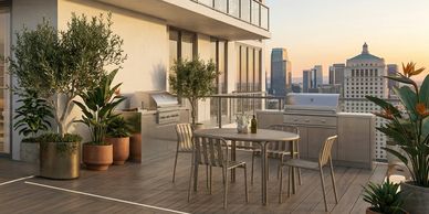 Modern rooftop patio with dining table, grill, and city skyline views at sunset.