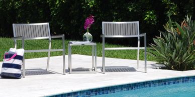 Two metal chairs and a small table by a pool with a flower vase on the table.