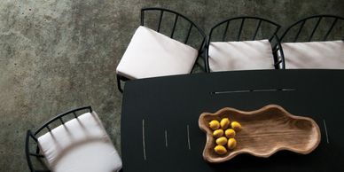Top view of a black table with cushioned chairs and a wooden bowl of lemons.