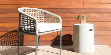 White woven chair and small table with plant against wooden wall.
