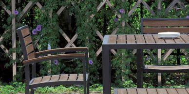 Wooden outdoor table and chairs in a garden with purple flowers.