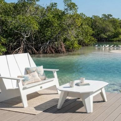 White outdoor furniture by a clear water body with greenery.