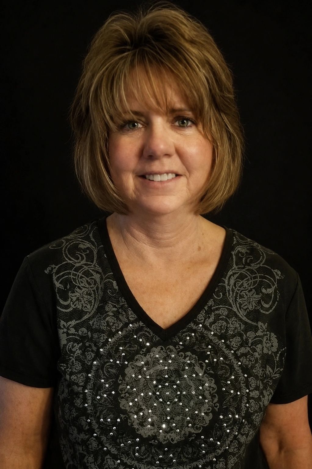 Smiling woman with short blonde hair in a black patterned shirt.
