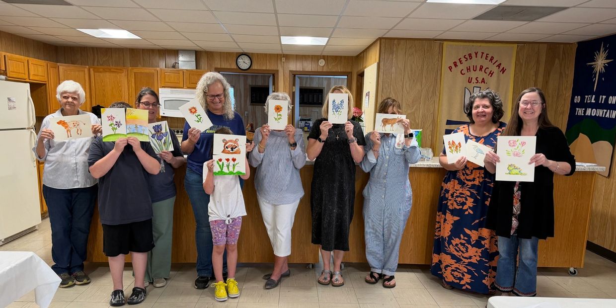 Group proudly displays their watercolor paintings in a cozy church hall.