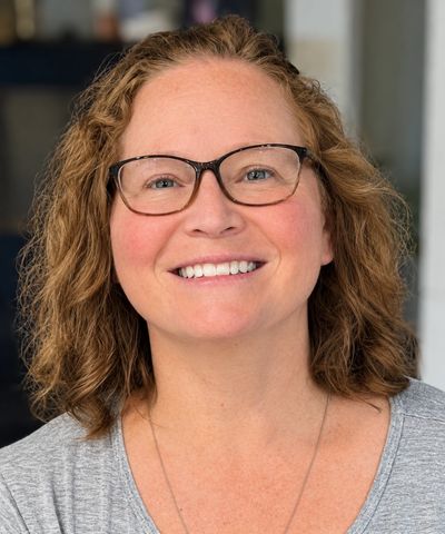 Smiling woman with glasses and curly hair.