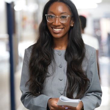 Confident woman with long hair and glasses smiling.