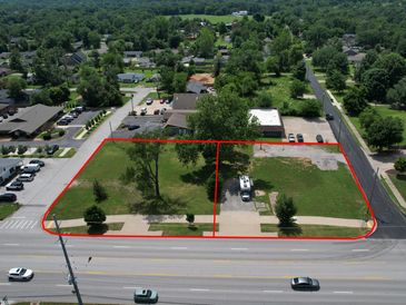 Two adjacent empty lots outlined in red next to a busy road.