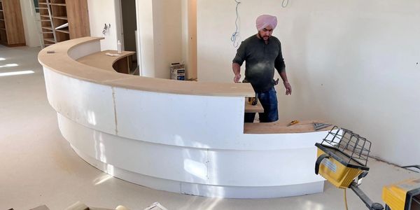 A man working on a curved wooden counter in a room under construction.