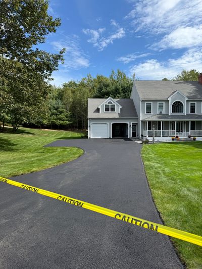 Newly paved driveway with caution tape in front of a suburban house.