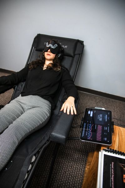 Woman relaxing on a chair with VR-like headset and tablet nearby.