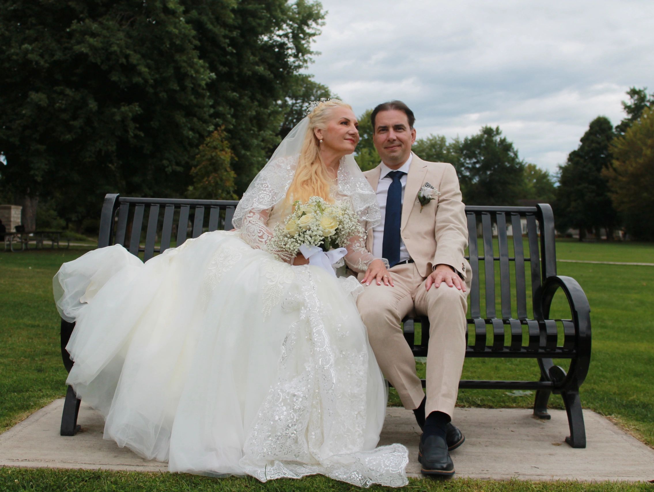 Newlywed couple sitting on a bench outdoors.