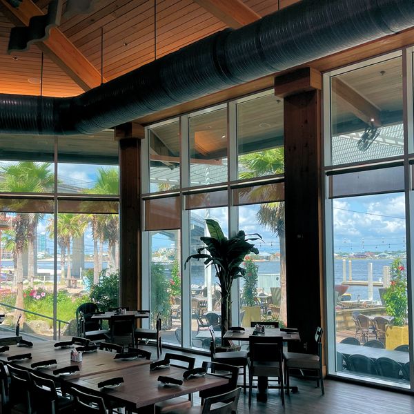 Spacious restaurant with large windows overlooking a waterfront patio and palm trees.