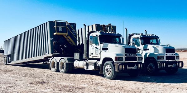 Two white Mack trucks parked side by side on a dirt lot under a clear blue sky.
