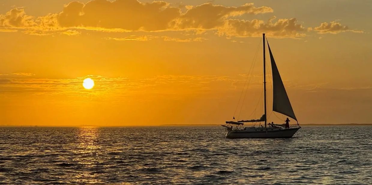 The sailboat ‘Courageous’ in the distance under a golden sunset sky on Charlotte Harbor, Florida