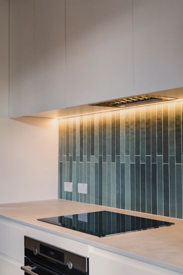 Modern kitchen with green tiled backsplash and induction cooktop.