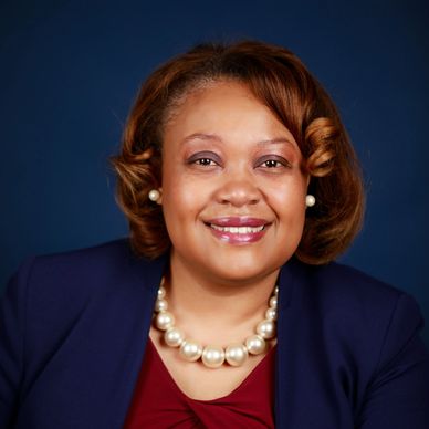 Smiling woman in professional attire with pearl necklace.