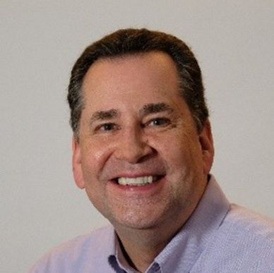 Smiling middle-aged man wearing a light purple shirt.