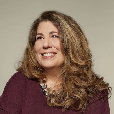 Smiling woman with long wavy hair wearing a purple top.