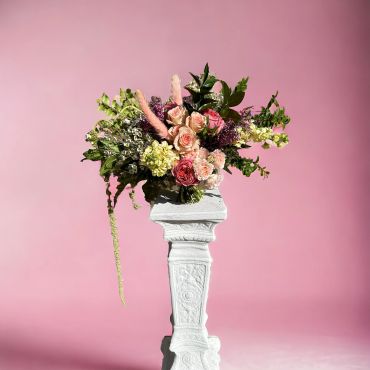 Elegant bouquet of roses and greenery on a white pedestal with a pink backdrop.