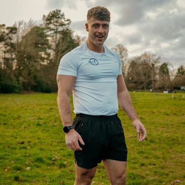 Athletic man in white shirt and black shorts standing outdoors on grass.