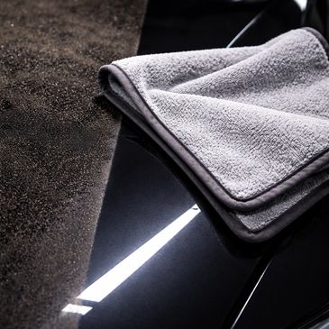 Gray microfiber towel on a shiny black surface with a dirty area beside it.