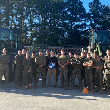 Group of military personnel posing outdoors with two tractors and a BMW logo.