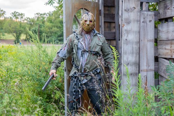 Person in a Jason Voorhees costume holding a machete in a field.