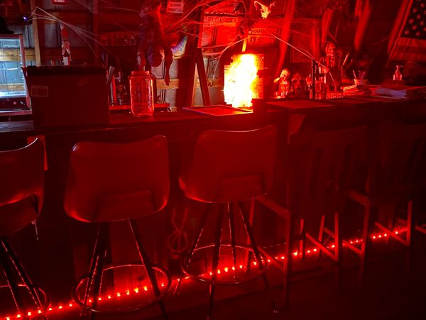 Dimly lit bar with red neon lights and empty stools.